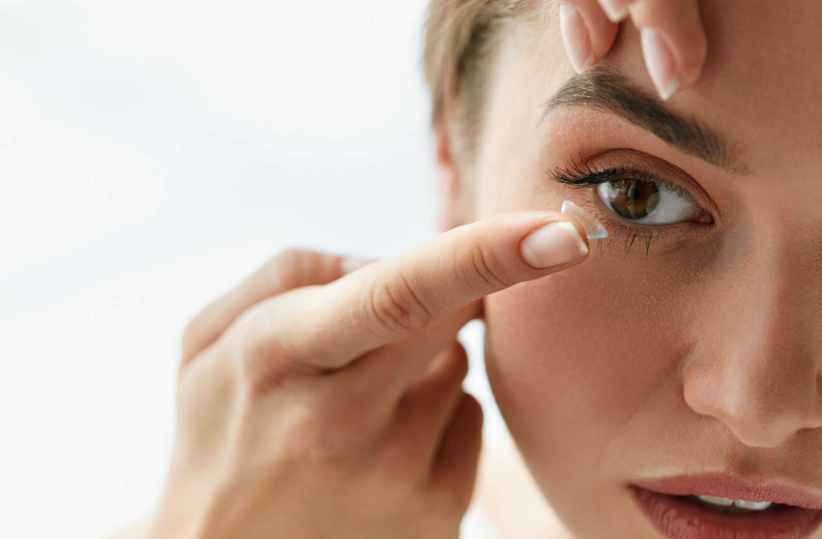A close-up of a woman putting a contact lens in her right eye.