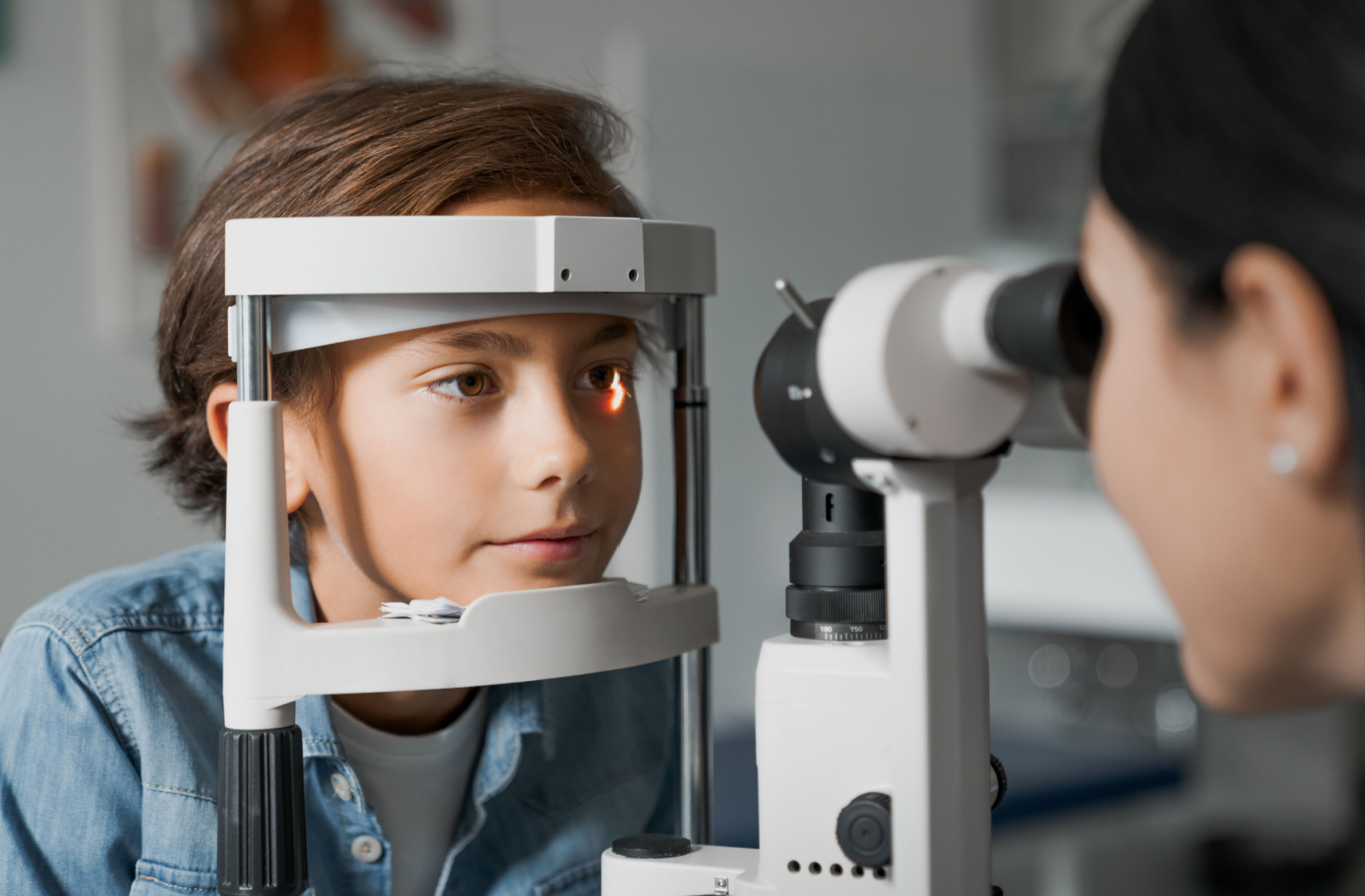 A young boy wearing a jean jacket undergoing a slit lamp test.