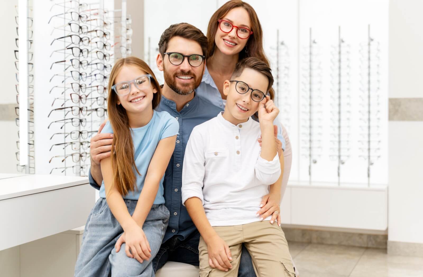 A happy family wearing glasses, posing inside an eyewear store with a display of frames in the background.